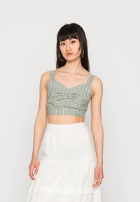 Top cropped de riscas verdes com textura tecida plana e alças largas, com um design de frente pregueada. Combinado com uma saia branca fluída.