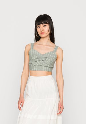 Top cropped de riscas verdes com textura tecida plana e alças largas, com um design de frente pregueada. Combinado com uma saia branca fluída.
