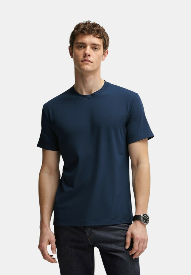 T-shirt blu navy a maniche corte realizzato in tessuto liscio con scollatura rotonda e cuciture minime, abbinato a jeans scuri e un orologio nero.