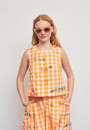 Narančasto-bijeli prsluk s kockastim uzorkom i šarenim natpisima, u kombinaciji s odgovarajućom suknjom koja ima džepove i udoban dizajn.