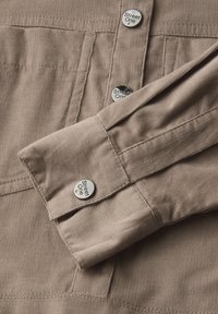 Beige kordfärg med en knapp-up krage, med silverknappar som har "Street One"-logotyp och manschettdetaljer.