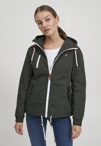 Grønn utendørsjakke med hette, som har en hvit glidelås foran, elastiske mansjetter og justerbare snorer. Inkluderer et teksturert logo-merke.