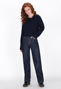 Pulover bleumarin cu guler în formă de fundă și mâneci lungi, combinat cu blugi negri cu croială largă și cizme negre până la gleznă. Stoff tricotat texturat.
