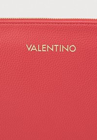 Κόκκινη δερμάτινη θήκη με υφή, χρυσή ένδειξη "VALENTINO" και επάνω φερμουάρ κλεισίματος.