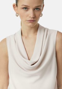 Jasnoróżowa bezrękawnikowa bluzka z drapowanym dekoltem i gładką teksturą materiału, z subtelnym połyskiem i minimalistycznym designem.