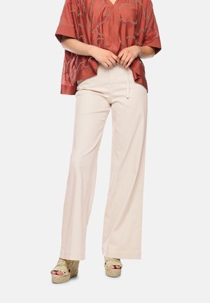 Person wearing wide-leg beige pants, a loose red patterned shirt, and beige woven wedge sandals, standing against a plain background.