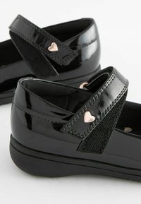 Schwarze Lacklederschuhe verfügen über elastische Riemen mit einem roségoldenen Herzakzent. Das Design ist schlank mit einer abgerundeten Zehenpartie und einer Plateau-Sohle.