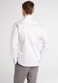 Weißes Langarmhemd mit structured Kragen, knöpfbaren Manschetten und kontrastierenden blauen Akzenten an den inneren Manschetten. Glattes Material, taillierte Passform.