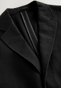 Sacou negru cu un guler neted, material texturat și pene interioare subtile cu un finisaj elegant. Design minimalist cu detalii lejer croite.