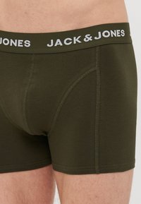 Olivgrüne Baumwoll-Boxershorts mit einem weißen Logo-Bündchen. Sie verfügen über ein enganliegendes Design und Kontrastnähte. Glatte Textur und elastischer Stoff.