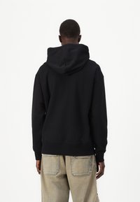 Sweatshirt à capuche noire avec une coupe décontractée, des poignets et un ourlet côtelés, et une texture lisse. La vue arrière montre un design minimal sans logos.