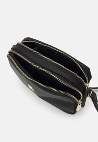Borsa a tracolla in pelle nera con tre scomparti con cerniera. Presenta una chiusura in metallo color oro e una texture liscia.