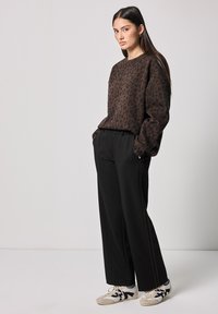 Felpa marrone con stampa leopardata, maniche lunghe, abbinata a pantaloni neri a gamba larga e sneakers bianche con accenti neri.