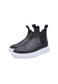 Botas de cuero negras hasta el tobillo con paneles laterales elásticos, que cuentan con lengüetas de tiro y una suela de goma blanca, mostrando un diseño elegante y minimalista.