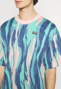 Tričko s krátkým rukávem v modré, azurové a růžové barvě s vlnkovým vzorem. Obsahuje růžový límeček a malé černé logo Adidas na hrudi.