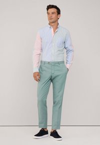 Overhemd met blauw en roze strepen, linkse zak; gecombineerd met lichtgroene broek en zwarte sneakers. Glad stof, getailleerde pasvorm.