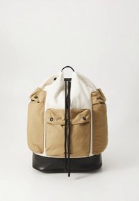 Reppu, jossa on kermaan vivahtava yläosa, vaaleanruskeat sivut ja musta pohja. Siinä on kaksinkertaiset sivutaskut, nyörikiristys ja kestävä pinta.