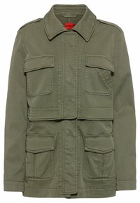 Veste cropped vert olive avec un col pointu, deux poches poitrine et deux poches à rabat inférieures ; fabriquée en tissu léger avec des coutures visibles.