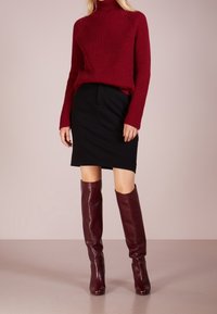 Pull à col roulé bordeaux côtelé associé à une jupe crayon noire et des bottes en cuir bordeaux montant jusqu'au genou, texture lisse et coupe ajustée.