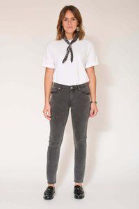 Jean skinny gris avec une texture lisse et un délavage subtil, porté avec un t-shirt blanc et une écharpe noire nouée autour du cou.