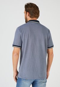 Polo in cotone grigio con una finitura leggermente texturizzata, caratterizzato da un colletto blu scuro e accenti a strisce sulle maniche. Visuale posteriore mostrata.