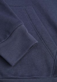 Felpa blu navy con tessuto testurizzato, polsini a coste e tasca frontale con dettagli di cucitura visibili. Design morbido e informale.