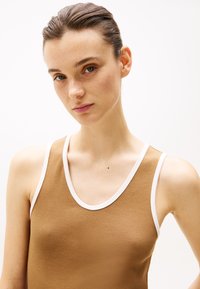 Débardeur marron à côtes avec finitions blanches, présentant une encolure dégagée et une coupe ajustée, porté par un modèle au teint naturel.