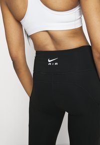 Czarne legginsy o wysokim stanie z teksturowanym wykończeniem, z białym logo "Nike AIR" na tylnym pasku i kontrastowymi szwami.