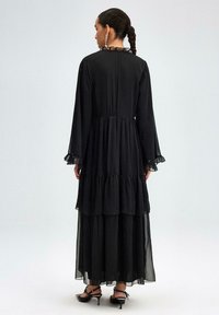 Black maxi dress with long, sheer sleeves and a tiered design. Features a lace-trimmed neckline and frilled sleeve hems. Smooth fabric texture.
