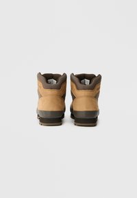 Scarpe da trekking in pelle marrone con colletto imbottito, suola in gomma grigia e dettagli testurizzati sulla parte superiore. I lacci non sono presenti in questa vista.