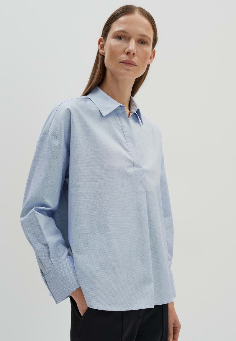 Camicia azzurro chiaro a maniche lunghe con collo a punta, caratterizzata da un tessuto texture, polsini con bottoni e una vestibilità rilassata. Design semplice e linee pulite.