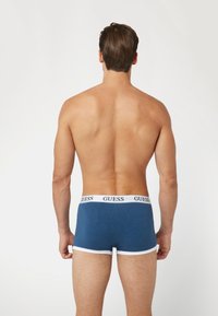 Bóxers azules con ribete blanco y una cinturilla con marca. Tela suave y diseño ajustado, vistos desde atrás en un torso desnudo.