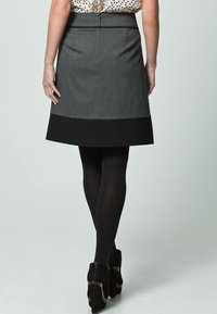 Grauer A-Linien-Rock mit schwarzem Saum, Reißverschluss und Rückennähten. Getragen mit schwarzen Strumpfhosen und heeled Stiefeletten. Gepunktetes Hemd sichtbar.