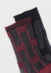 Ζευγάρι ημιδιαφανών κάλτσων, μία μαύρη και μία γκρι με μπορντό ρίγες και επαναλαμβανόμενα μοτίβα κειμένου "HUGO".