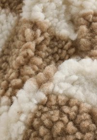 Tekstil af uld med tekstur i beige og hvide nuancer, der har en blød og fluffy overflade med varierende tufter og bløde, fuzzy fibre.