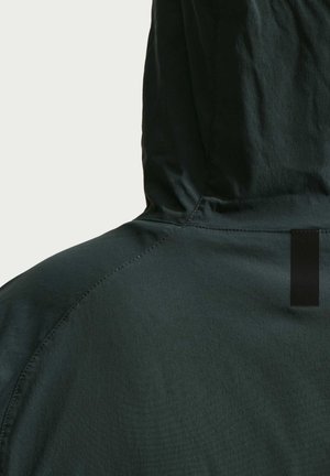Hættetrøje i mørkegrønt stof. Indeholder en struktureret overflade, kontrastfuldt sort label og syningsdetaljer langs skuldrene.