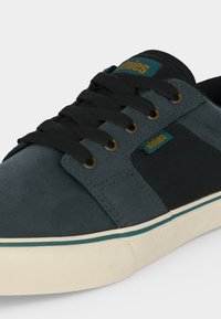 Baskets bleu sarcelle foncé et noir avec lacets noirs, œillets dorés, semelle blanche avec bande sarcelle et étiquettes de marque « etnies » sur la languette et le côté.