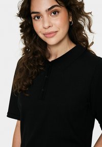 Mustapaita, jossa on ribbbitekstuuri, kauluksessa ja kolmessa napissa varustettu kaulus. Lyhyet hihat, joissa on käärityt hihansuut.