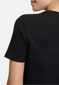 Schwarzes, strukturiertes Kurzarmshirt mit einem runden Ausschnitt, das dezente Sprenkel im Stoff aufweist. Einfaches, klares Design.