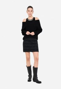 Maglione nero scollato spalle, gonna con motivo testurizzato e stivali neri alti fino al ginocchio con dettagli in metallo. Palette di colori semplice, design moderno.