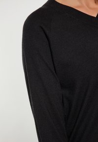 Pulover negru din tricot, cu decolteu în V și mâneci lungi, având o textură netedă și o croială clasică.