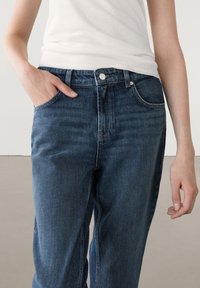 Donkerblauwe denim jeans met een rechte snit, vijf zakken en een knoopsluiting. Gladde textuur met zichtbare stikseldetails.