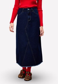 Jupe midi en denim bleu foncé avec coutures avant et ourlet effiloché, dotée d'une fermeture à boutons et de poches, associée à des chaussures à imprimé léopard marron.