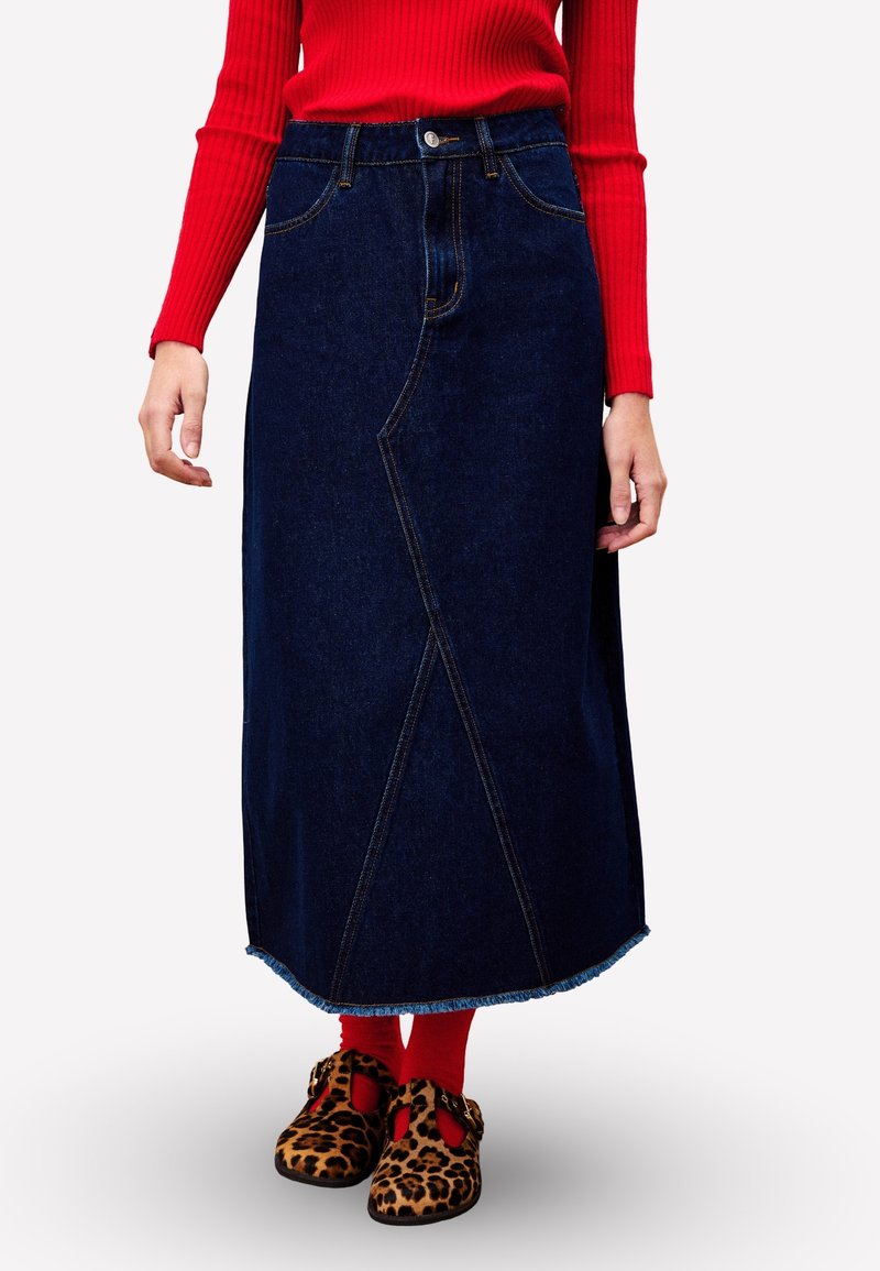 Jupe midi en denim bleu foncé avec coutures avant et ourlet effiloché, dotée d'une fermeture à boutons et de poches, associée à des chaussures à imprimé léopard marron.