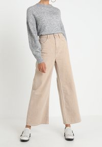 Ljusgrå stickad tröja, beige vida kordbyxor, vita skor med svarta detaljer. Slät textur, avslappnad passform och högmidjad design.