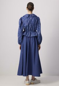 Blusa blu con motivo a fantasia, maniche a sbuffo, vita a peplum e una gonna lunga coordinata. Indossata con sneakers bianche, dotate di suola piatta.