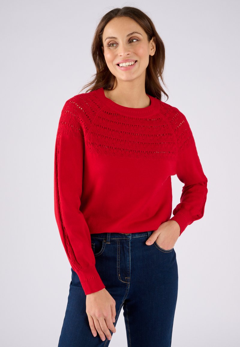 Maglione rosso lavorato a maglia con un giromanica testurizzato, caratterizzato da un design a reticolo sulle maniche. Abbinato a jeans blu, che mostrano un fit rilassato.