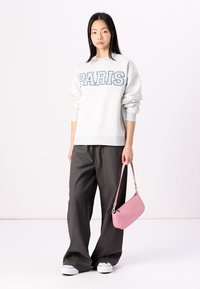 Felpa grigia chiara con la scritta "PARIS" in lettere blu, abbinata a pantaloni larghi grigio scuro e una borsa rosa testurizzata. Sneakers bianche semplici.