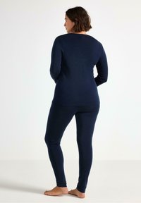 Sæt bestående af en navyblå langærmet top og leggings, lavet af blødt stof, med rund halsudskæring og tætsiddende design, set fra ryggen.