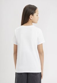 T-shirt bianca in cotone con maniche corte e scollo tondo, caratterizzata da una trama liscia e un design semplice e minimalista.